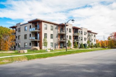 New apartment building surrounded by colourful autumn trees in a housing development on a partly clody day. Huntsville, ON, Canada. clipart