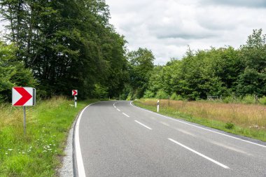 Bulutlu bir yaz gününde, orman boyunca bir kır yolu boyunca keskin bir virajın fotoğrafı.