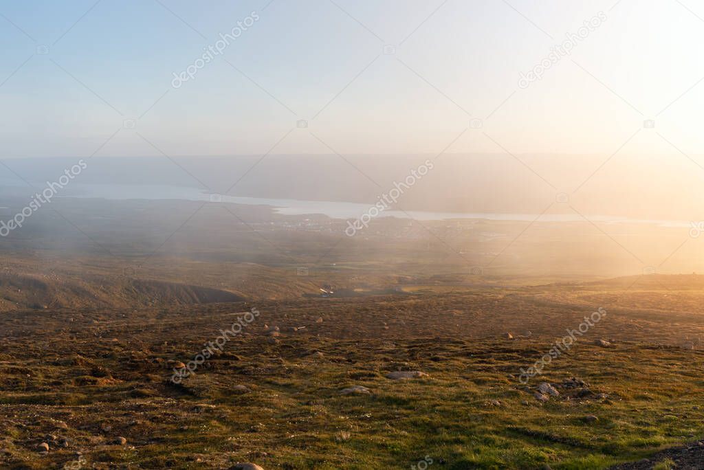 View of a broad valley with a large lake covered with fog as seen from the top of a mountain at sunset. Egilsstadir, Iceland.
