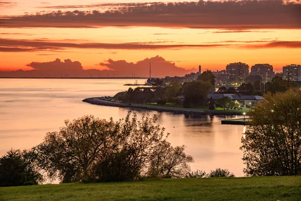 火热的落日笼罩着湖上的市中心 一个有高风力涡轮机的岛屿在背景上是可见的 加拿大 金斯敦 — 图库照片