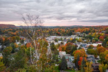 Günbatımında sonbahar renklerinin zirvesinde bir ormanla çevrili küçük bir kasabadaki ticari binaların üzerindeki görüntüye bakın. Huntsville, On, Kanada.