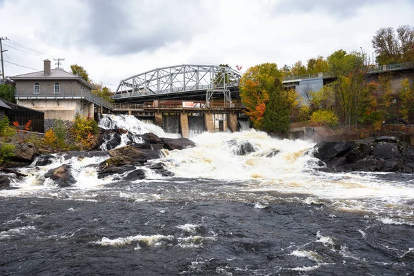 Water spilling over the top of a small dam at a hydroelectric power plant along a river on a cloudy Autumn Day. Ontario, Canada.