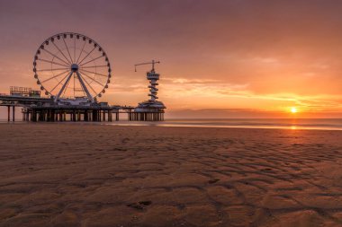 Yazın gün batımında kumlu bir sahil boyunca bir rıhtımda dönme dolap. Scheveningen Sahili, Lahey, Hollanda.