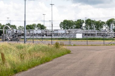 Kuyu başları ve boru hatları bulutlu bir yaz gününde kırsal bölgedeki bir doğalgaz çıkarma sahasında. Groningen gaz sahası, Hollanda....