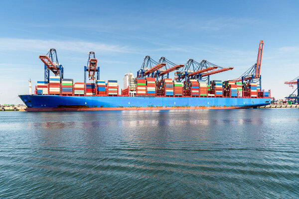 Container ship being loaded while docked to a container terminal with tall gantry cranes on a sunny summer day. Port of Rotterdam, the Netherlands.