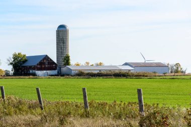 Farm with an old barn and a silo at the far end of a grassy field on a sunny autumn day. A wind turbine is visible in background. Wolfe Island, ON, Canada.