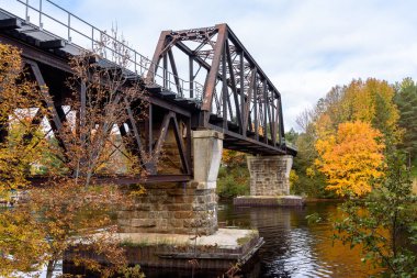 Low angle view of an old steel railroad bridge spanning a narrow river on a cloudy autumn day. Huntsville, ON, Canada.