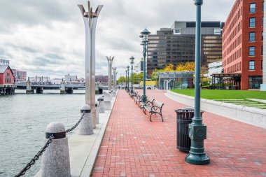 Empty brick waterfront footpath lined with benches and lamp post on a cloudy autumn day. Boston, MA, USA.