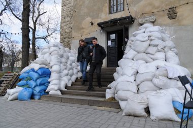 Lviv, Ukrayna 4 Nisan 2022. Rusya 'nın işgali sırasında insanlar Lviv' deki bir binanın önündeki kum torbası barikatının önünden geçiyorlar. Rusya 24 Şubat 2022 'de Ukrayna' yı işgal etti ve 2. Dünya Savaşı 'ndan bu yana Avrupa' daki en büyük askeri saldırıyı tetikledi..