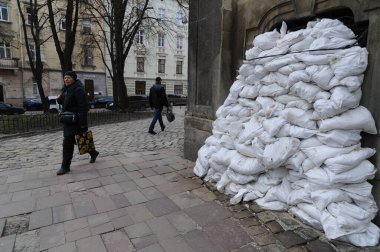 Lviv, Ukrayna 4 Nisan 2022. Rusya 'nın işgali sırasında insanlar Lviv' deki bir binanın önündeki kum torbası barikatının önünden geçiyorlar. Rusya 24 Şubat 2022 'de Ukrayna' yı işgal etti ve 2. Dünya Savaşı 'ndan bu yana Avrupa' daki en büyük askeri saldırıyı tetikledi..