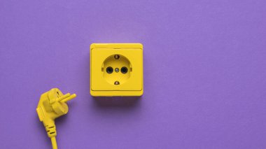 Fişi olan sarı bir elektrik kablosu ve mor arka planda sarı bir soket. Şık tasarım. Elektrikli aletlerin bağlı olduğu yer..