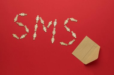 Tahta adamlardan yapılmış SMS yazıtları ve kırmızı arka planda açık bir posta kağıdı zarfı. İnsanlar arasındaki iletişim kavramı.