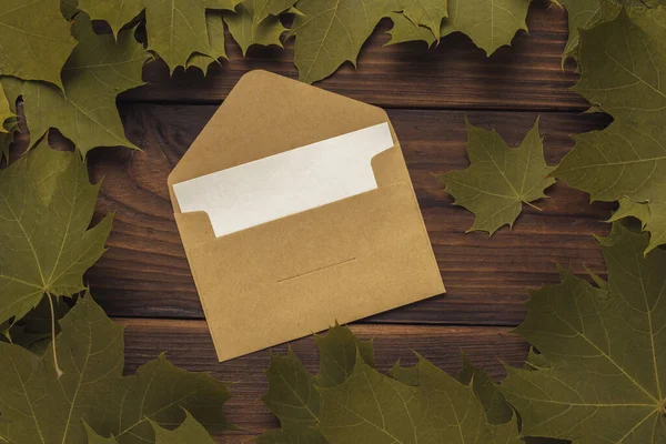 一个开着的信封 有一张纸片 在木制背景上的叶框里 秋天的心情2 来往公文 — 图库照片