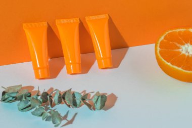 Bir tutam okaliptüs, üç tüp krema ve beyaz ve turuncu arka planda bir portakal. Kozmetik kremler.