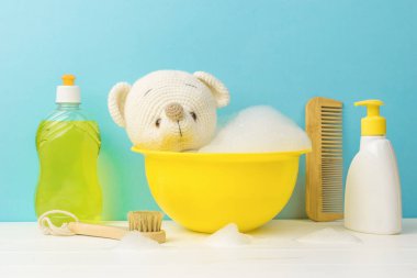 Bir tarak, deterjan ve sarı bir leğende yıkanan örülmüş bir oyuncak ayı. Küçük çocukları yıkama konsepti.