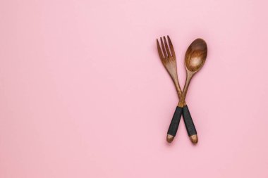 Pembe arka planda klasik ahşap kaşık ve çatal. Mesaj için yer var. Düz yatıyordu.
