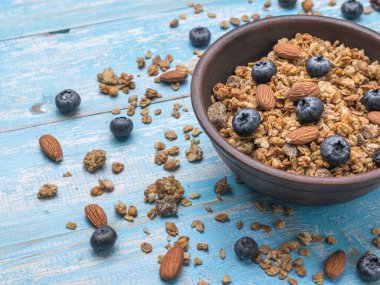 Mavi bir masanın üzerinde fındık, böğürtlen ve müsli olan derin bir kase. Sağlıklı vejetaryen kahvaltısı.