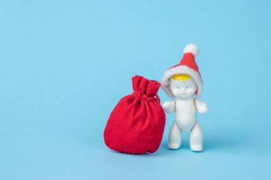 Kırmızı şapkalı bir bebek heykeli ve mavi arka planda hediyeler olan bir çanta. Minimalizm. Yeni yıl konsepti.