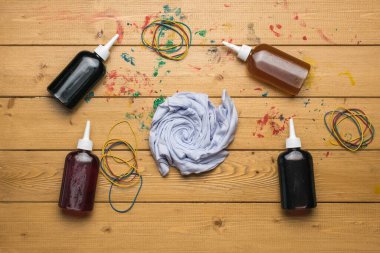 Four bottles of paint and a white T-shirt rolled up for coloring in tie dye style. The process of painting in the style of tie dye. Flat lay. clipart