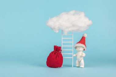 Kırmızı şapkalı bir bebek figürü ve bulutun üzerinde duran bir merdiven. Noel Baba 'dan sürpriz konsepti. Yeni yılın modası bu. Minimalizm.