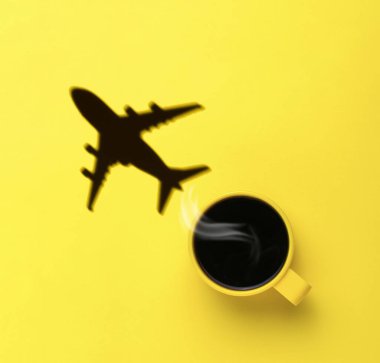 Sarı bir arka planda sarı bir kahve fincanından uçan bir uçağın gölgesi. Seyahat ve hava taşımacılığı konsepti. Düz yatıyordu.