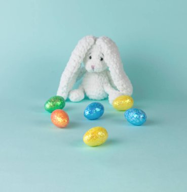 Colorful Easter eggs and a knitted rabbit in the background. The concept of Easter.