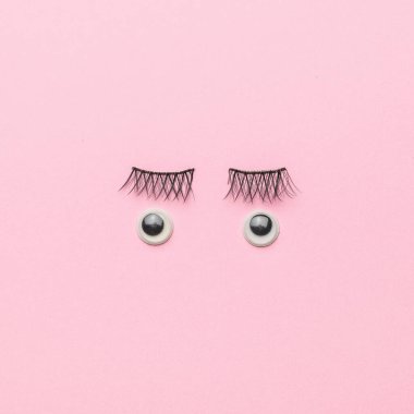 Big eyelashes and doll eyes on a pink background. Without a face. Flat lay.