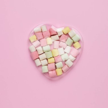 Marshmallow in a transparent heart-shaped package on a pink background. The concept of Valentine's Day. Flat lay.