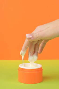 A girl taking a cosmetic cream from an orange jar. The concept of using cosmetics.