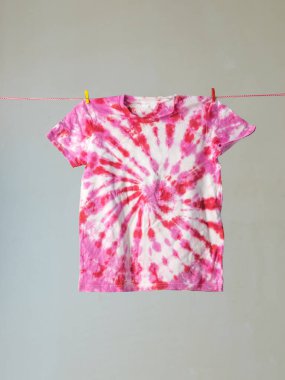 Abstract tie dye style drawing on a T-shirt hanging on a clothesline. Production of dyed clothing. clipart