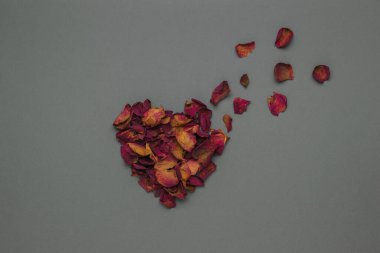 Kurumuş kırmızı gül yapraklarından oluşan uçan bir kalp. Romantik ilişki kavramı. Düz yatıyordu.