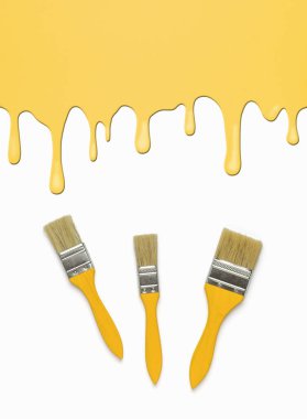 Ahşap saplı üç fırça ve akan boyanın etkisiyle sarı bir arka plan. Moda rengi. Düz yatıyordu.