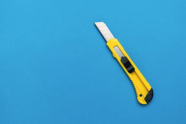 Mavi arka planda katlanmış büyük bir kırtasiye bıçağı. Mesajın için bir yer. Yaratıcılık ve eğitim araçları. Düz yatıyordu.