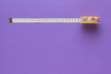 Mor arka planda mezurası olan bir bobin. Vücut parametrelerini ölçen bir cihaz. Düz yatıyordu. Renk trendi. Metin için yer.