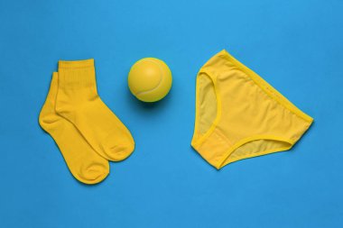 Sarı çoraplar, tenis topu ve mavi arka planda külotlar. Kadın sporları konsepti. Düz yatıyordu.