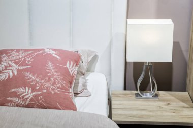 Yatak odasının içi, yastıklı yatak ve battaniyeli, lamba komodinin üstünde.