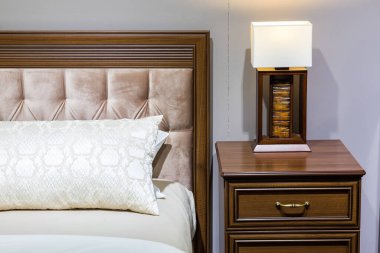 Yatak odasının içi, yastıklı yatak ve battaniyeli, lamba komodinin üstünde.