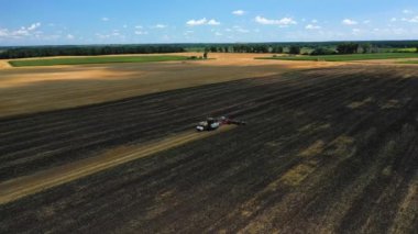 The tractor works the soil after the harvest at the summer day aerial view