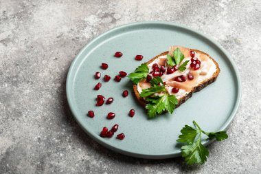 Jambonlu sandviç, otlar ve mavi tabakta nar ve yakın plan gri arka plan görüntüsü.