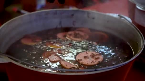 Glühwein wordt gekookt in een steelpan. De kok voegt kruidnagel toe aan het kokende drankje. — Stockvideo