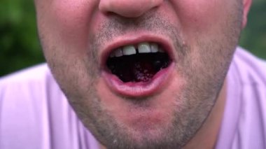 male chews blueberries painted tongue close-up.
