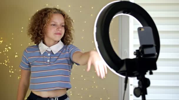 Jonge Blogger Concept. Vrolijke tiener meisje dansen op camera filmen video met behulp van de telefoon op statief thuis, het creëren van haar trendy content op een mobiele app om te delen op sociale media. — Stockvideo