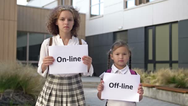 Två skolflickor med plakat står framför skolbyggnaden. En affisch i händerna på en liten flicka. Tonårstjej innehar en affisch ON-LINE. — Stockvideo