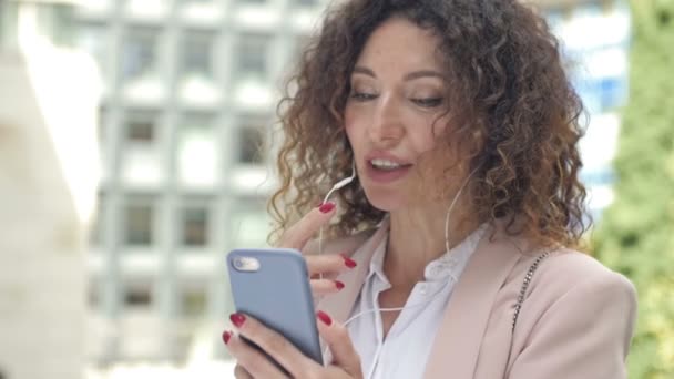 Portrait d'une femme d'affaires capable de travailler dans une rue de la ville avec un téléphone et un casque. Marchez dehors et travaillez dehors. Nouveau mode de vie normal. — Video