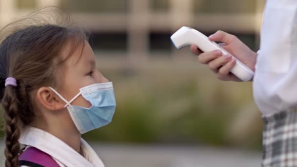 戴防护面罩的小女生要检查温度。大流行病期间的预防措施. — 图库视频影像