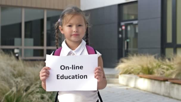 Söt liten skolflicka med flätor står med en affisch ON-LINE UTBILDNING — Stockvideo