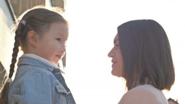 Genç bir kadın, 6-7 yaşlarında örgülü bir kıza sevgiyle sarılıyor. Anne ve kızının tanışması ya da ayrılması. Anneler Günü.