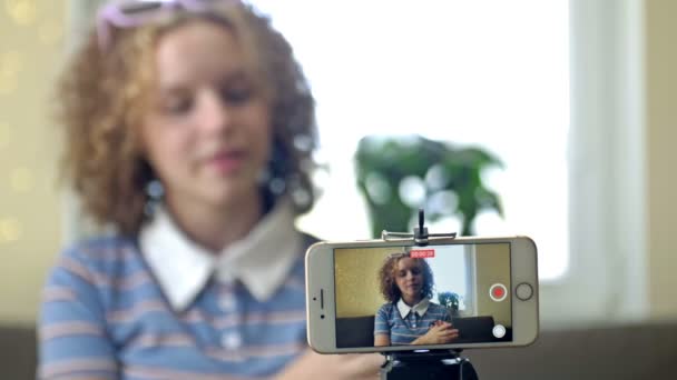 Young Blogger Concept. Chica adolescente alegre filmando vídeo usando el teléfono en el trípode en casa, creando su contenido de moda en una aplicación móvil para compartir en las redes sociales. — Vídeos de Stock