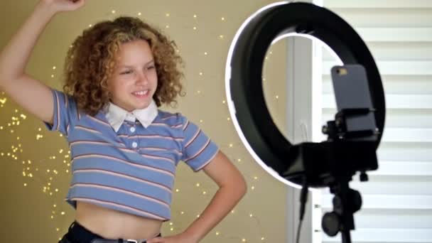 Young Blogger Concept. Fröhliches Teenie-Mädchen, das vor der Kamera tanzt, filmt das Video mit dem Handy auf einem Stativ zu Hause und erstellt ihre trendigen Inhalte auf einer mobilen App, um sie in den sozialen Medien zu teilen. — Stockvideo