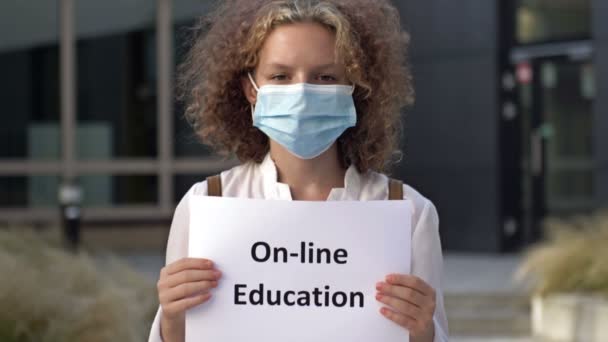 Μαθήτρια που φοράει ιατρική μάσκα κρατά ένα σημάδι ON-LINE ΕΚΠΑΙΔΕΥΣΗ. — Αρχείο Βίντεο